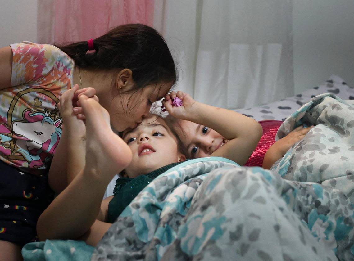 Rachel, 7, kisses her sister Katherin Leyva, 5, center, while she lays in bed with their other sister, Evelyn, 3, on Thursday, Dec. 1, 2022, in Hialeah. Katherin is diagnosed with Autism Spectrum Disorder. The family lost the majority of their possessions in a fire.
