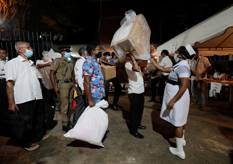 A health official takes the temperature of election officials who arrive with ballot boxes from a polling station to a counting center, after the voting ended during the country's parliamentary election in Colombo
