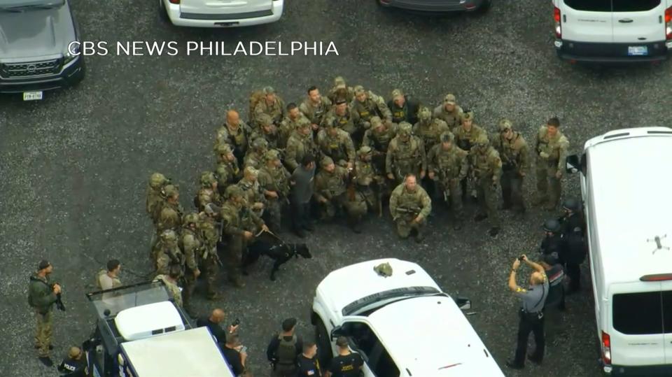 In this image from video provided by CBS NEWS Philadelphia, law enforcement officers pose for a group photo with Danelo Cavalcante after his capture in rural Pennsylvania on Wednesday, Sept. 13, 2023. The murderer who brazenly escaped from a Pennsylvania jail was captured in the woods by a team of tactical officers, bringing an end to an intensive search that terrified residents as the fugitive broke into homes for food, changed his appearance and stole a van and rifle during two weeks on the run. (CBS NEWS Philadelphia KYW-TV via AP) ORG XMIT: NYSS311