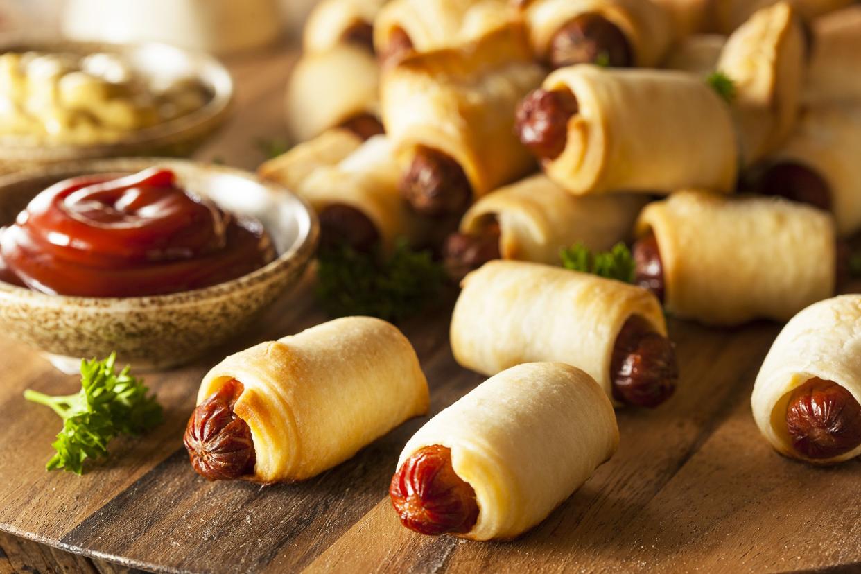 Several piglets in the blanket on a wooden cutting board with ketchup and mustard with a blurred background