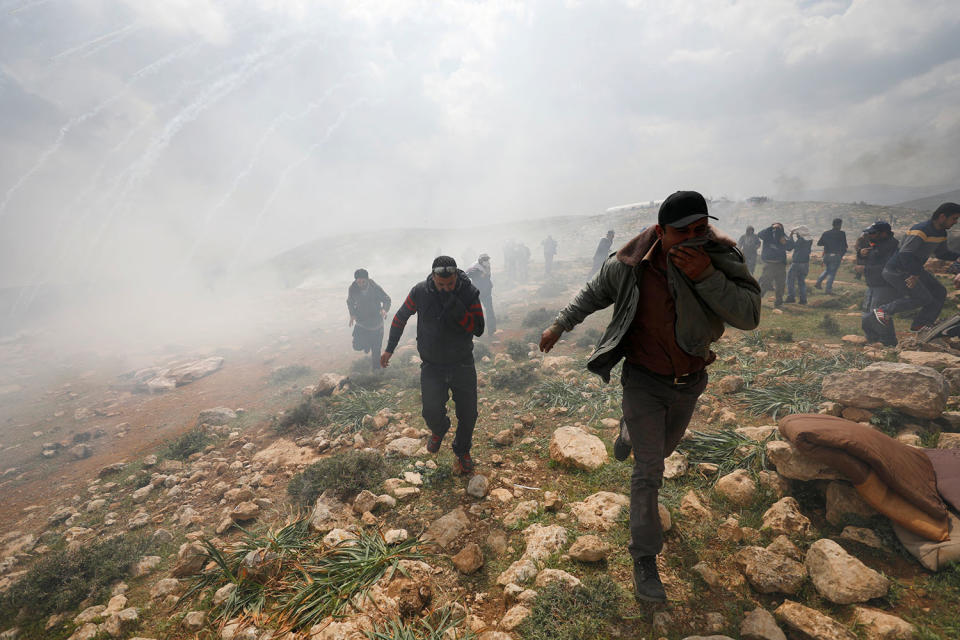 Palestinian protesters run for cover from tear gas