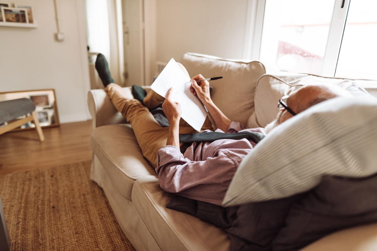 senior man writing a document lying down in the sofa