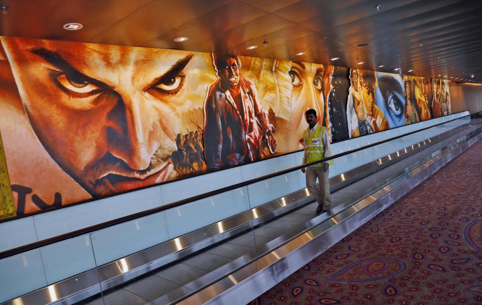 In this Wednesday, Jan. 8, 2014 photo, a worker walks near paintings of Bollywood stars displayed on the wall of the new airport terminal at the Chhatrapati Shivaji International Airport in Mumbai, India. India's overcrowded financial capital unveils its long-awaited $2 billion new airport terminal Friday, an ambitious, art-filled space that developers hope will be a showcase success in a country struggling to modernize inadequate infrastructure that is holding back economic growth. (AP Photo/Rajanish Kakade)