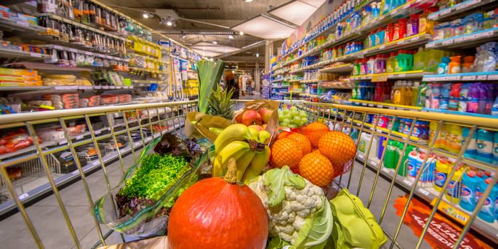 A cart filled with produce in a grocery aisle.