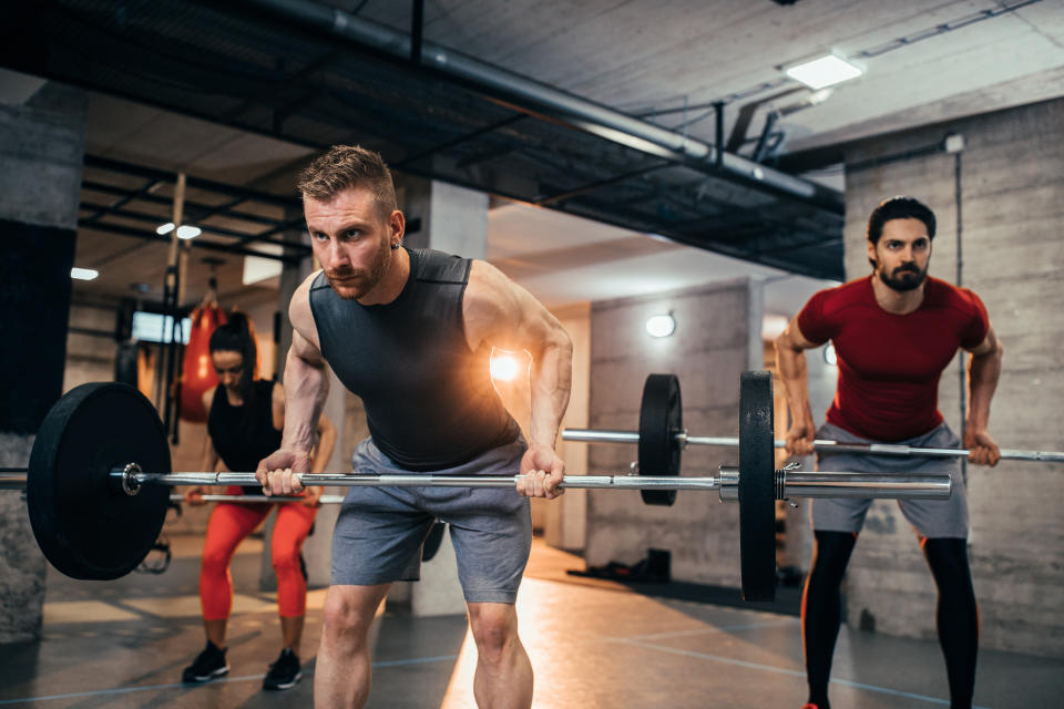 Shot of two young men and a woman lifting weights at the gym