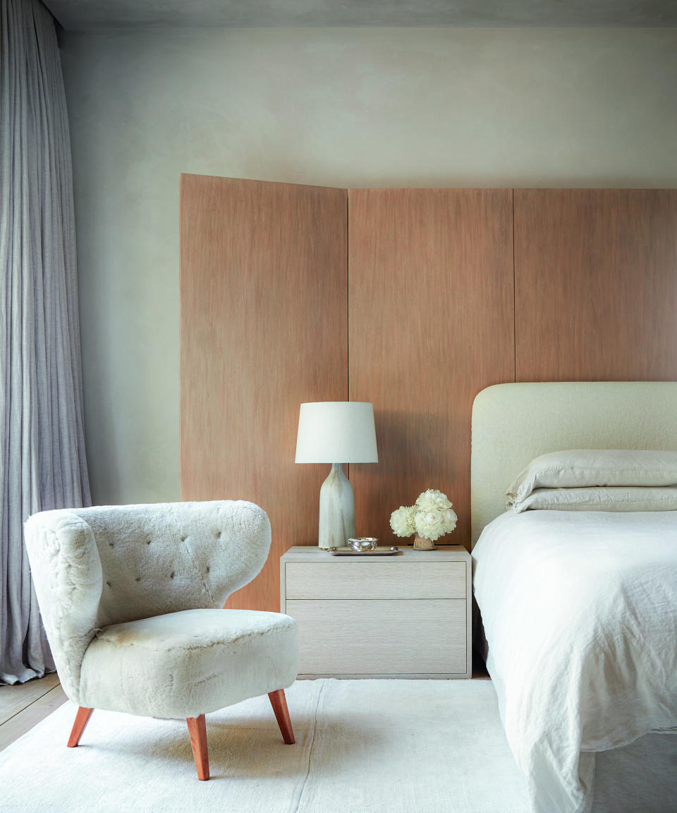 white bedroom with white 1940s sheepskin chair, white bed, wooden screen, white rug and lamp and bedside drawers