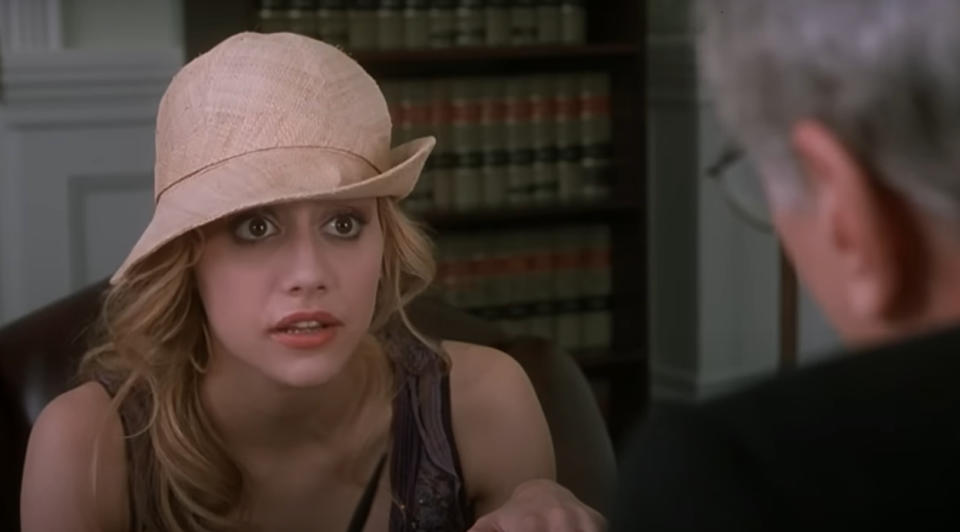 Brittany Murphy, wearing a hat, looks surprised while seated and talking to an older man in an office.