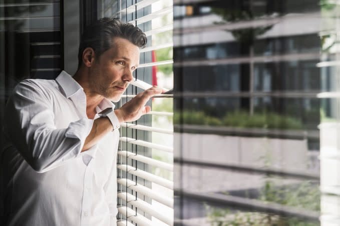 Businessman peeking through sunblinds at the window in office