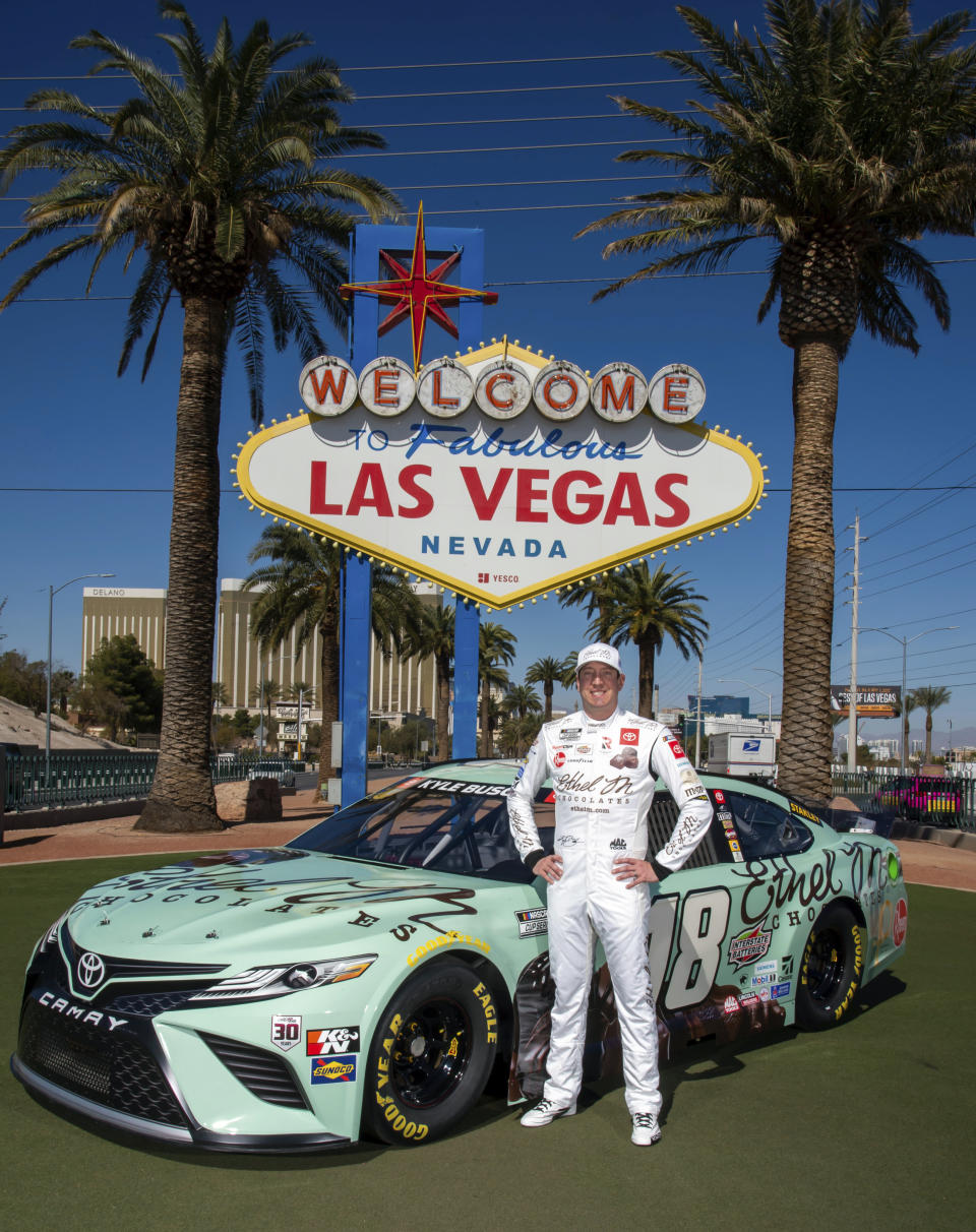 In this image provided by Ethel M Chocolates, NASCAR driver Kyle Busch poses in front of the famous "Welcome to Fabulous Las Vegas" sign with his Ethel M Chocolates sponsor race car in Las Vegas. Busch first went to the Ethel M candy factory with his grandmother. It wasn’t a tourist stop to the young Busch, it was a candy store and his grandmother let him roam the cactus garden and rewarded him with the craft chocolates. Ethel M is part of the Mars Corp., the longtime sponsor of Busch’s team. Busch will feature the brand on his car in Sunday’s race. (Christian Andrade-Cashman/Ethel M Chocolates via AP)