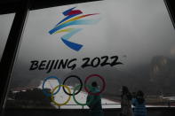 Visitors stand near a logo for the 2022 Beijing Winter Olympics at a ski resort in Yanqing on the outskirts of Beijing, China, Thursday, Dec. 23, 2021. Richer, more heavily armed and openly confrontational, China has undergone history-making change since the last time it was an Olympic host in 2008. (AP Photo/Ng Han Guan)