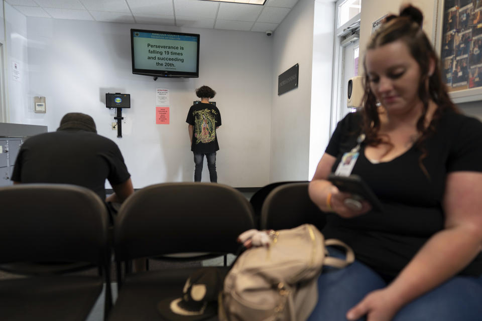 A person signs in, center, as Jesse Johnson of the Family Resource Center, right, waits for client Tyler Baker to complete a random drug test at the Hancock County Adult Probation office in Findlay, Ohio, Thursday, Oct. 12, 2023. Experts say establishing peer support programs to help people in recovery is one way communities should consider using money from settling lawsuits with the drug industry over the toll of opioids. (AP Photo/Carolyn Kaster)