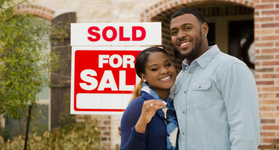 A man and a woman standing in front of a 'sold' house sign.