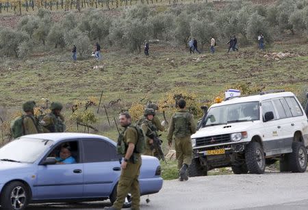 Israeli soldiers stand guard as Palestinians walk away from the scene of what the Israeli army said was a suspected Palestinian stabbing attack, near the West Bank Al-Fawwar refugee camp, south of Hebron November 25, 2015. REUTERS/Mussa Qawasma