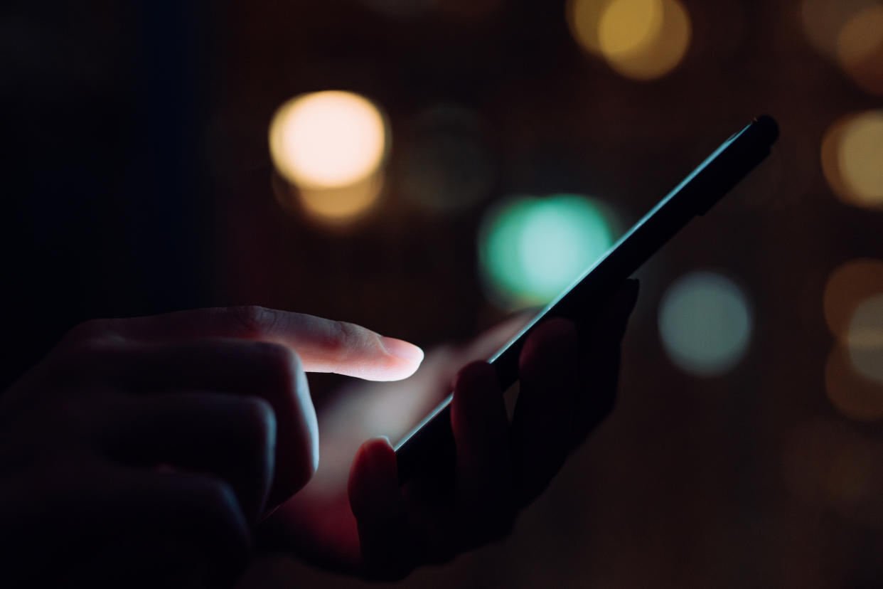 Apple Close up of woman's hand using smartphone in the dark, against illuminated city light bokeh