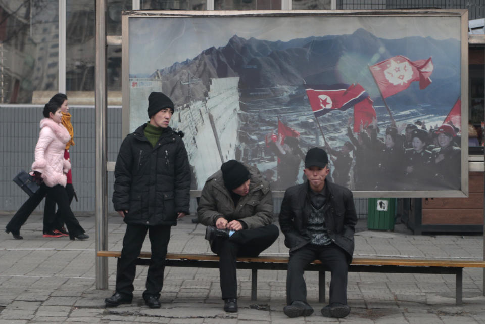 In this Nov. 26, 2019, photo, men wait for public transport near a propaganda photo showing North Korean 'soldiers-builders' in downtown Pyongyang, North Korea. North Korean leader Kim Jong Un and U.S. President Donald Trump have signaled their affection for each other so regularly it might be easy to miss rising fears that the head-spinning diplomatic engagement of the past two years is falling apart. (AP Photo/Dita Alangkara)