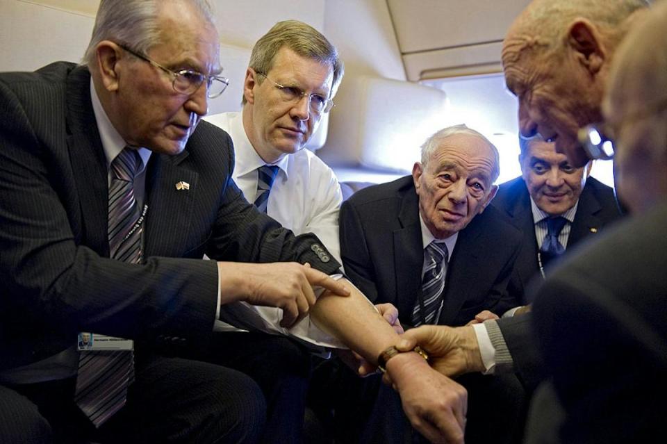 Hermann Hoellenreiner, a Sinto Holocaust survivor, shows his prisoner tattoo to David Lewin, a Jewish Holocaust survivor, as they and officials travel to a commemoration ceremony in 2011. <a href="https://www.gettyimages.com/detail/news-photo/german-president-christian-wulff-looks-on-as-sinto-news-photo/108426185?adppopup=true" rel="nofollow noopener" target="_blank" data-ylk="slk:Jesco Denzel/AFP via Getty Images;elm:context_link;itc:0;sec:content-canvas" class="link ">Jesco Denzel/AFP via Getty Images</a>