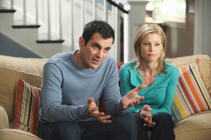 Ty Burrell and Julie Bowen sit on a couch in casual outfits during a scene from the show "Modern Family"