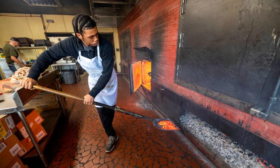 Nkosi Barnes, places hardwood coals beneath the pork shoulders cooking at Lexington Barbecue on Tuesday, October 10, 2023 in Lexington, N.C.