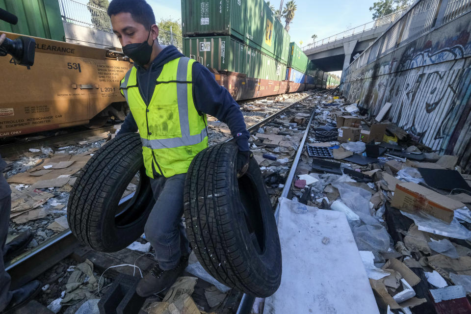 Contractor worker Luis Rosas removes vehicle tires from the shredded boxes and packages along a section of the Union Pacific train tracks in downtown Los Angeles Friday, Jan. 14, 2022. Thieves have been raiding cargo containers aboard trains nearing downtown Los Angeles for months, leaving the tracks blanketed with discarded packages. The sea of debris left behind included items that the thieves apparently didn't think were valuable enough to take, CBSLA reported Thursday. (AP Photo/Ringo H.W. Chiu)