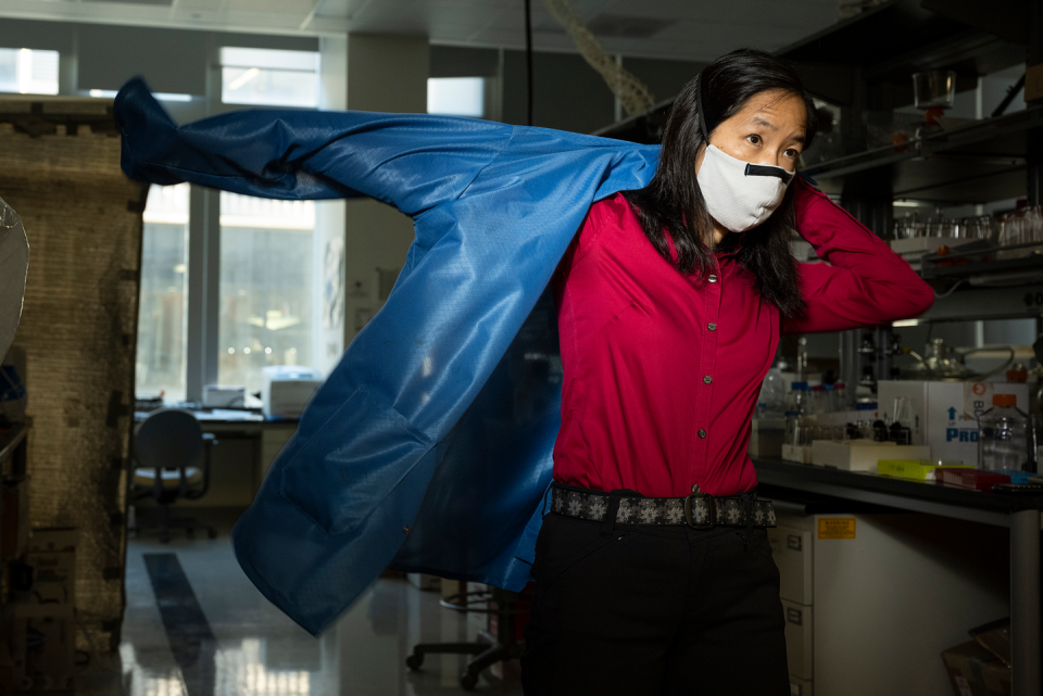 scientist marr in the lab putting on her lab jacket with a face mask on