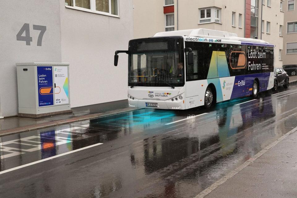 An electric bus painted in black and white drives down a wet road in Germany.