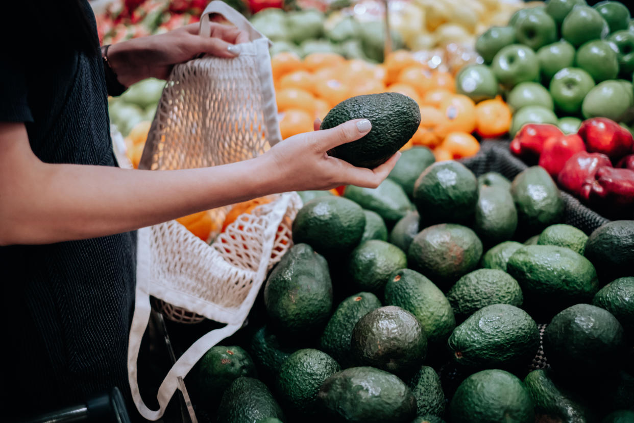 A woman shopping for produce at a supermarket with a mesh bag.