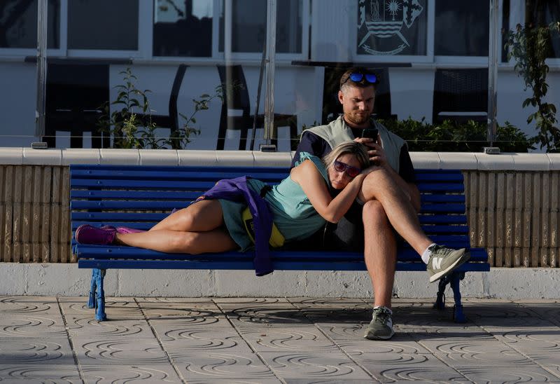 FILE PHOTO: A couple sits on a bench as they enjoy the sun in front of the sea during unseasonably warm temperatures in Malaga