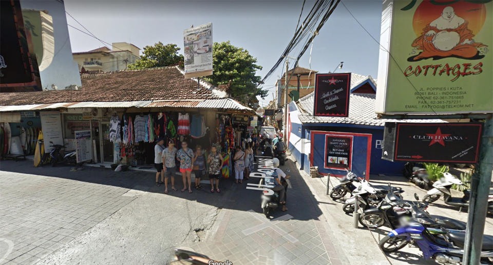 Tourists stand outside a colourful clothing shop as scooters drive past in Bali.