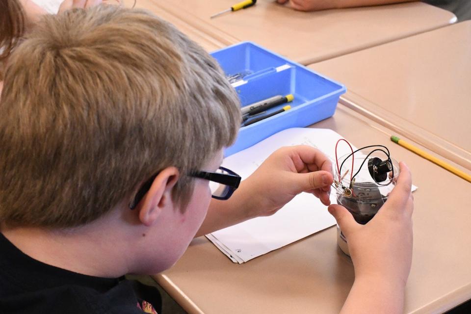 A student adds a paperclip to act as the switch, completing the circuit which he has wired in his plastic bottle flashlight.