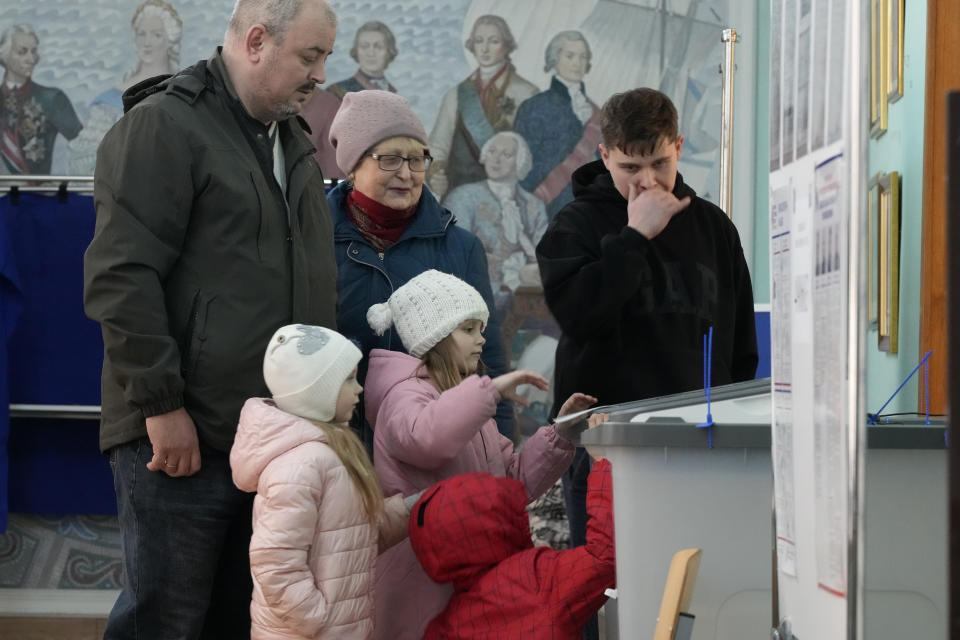 A family votes at a polling station located in a school during the presidential elections in St. Petersburg, Russia, Saturday, March 16, 2024, with a painting depicting the Russian Tsarina Catherine II and her contemporaries on the wall. Voters in Russia are heading to the polls for a presidential election that is all but certain to extend President Vladimir Putin's rule after he clamped down on dissent. (AP Photo/Dmitri Lovetsky)