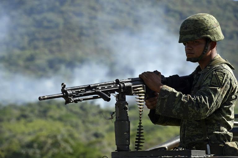 A soldier of the 88 infantry brigade patrols as smoke raises after a military helicopter was shot down in Villa Vieja community, Villa Purificacion, Jalisco State, Mexico on May 2, 2015