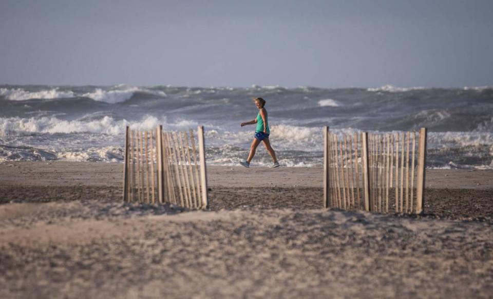 A woman walks down a windy shoreline in Atlantic Beach, N.C. on Tuesday morning, Aug. 4, 2020, in the hours after Hurricane Isaias, which later became a tropical storm, brought heavy winds and rain, but caused minimal damage.