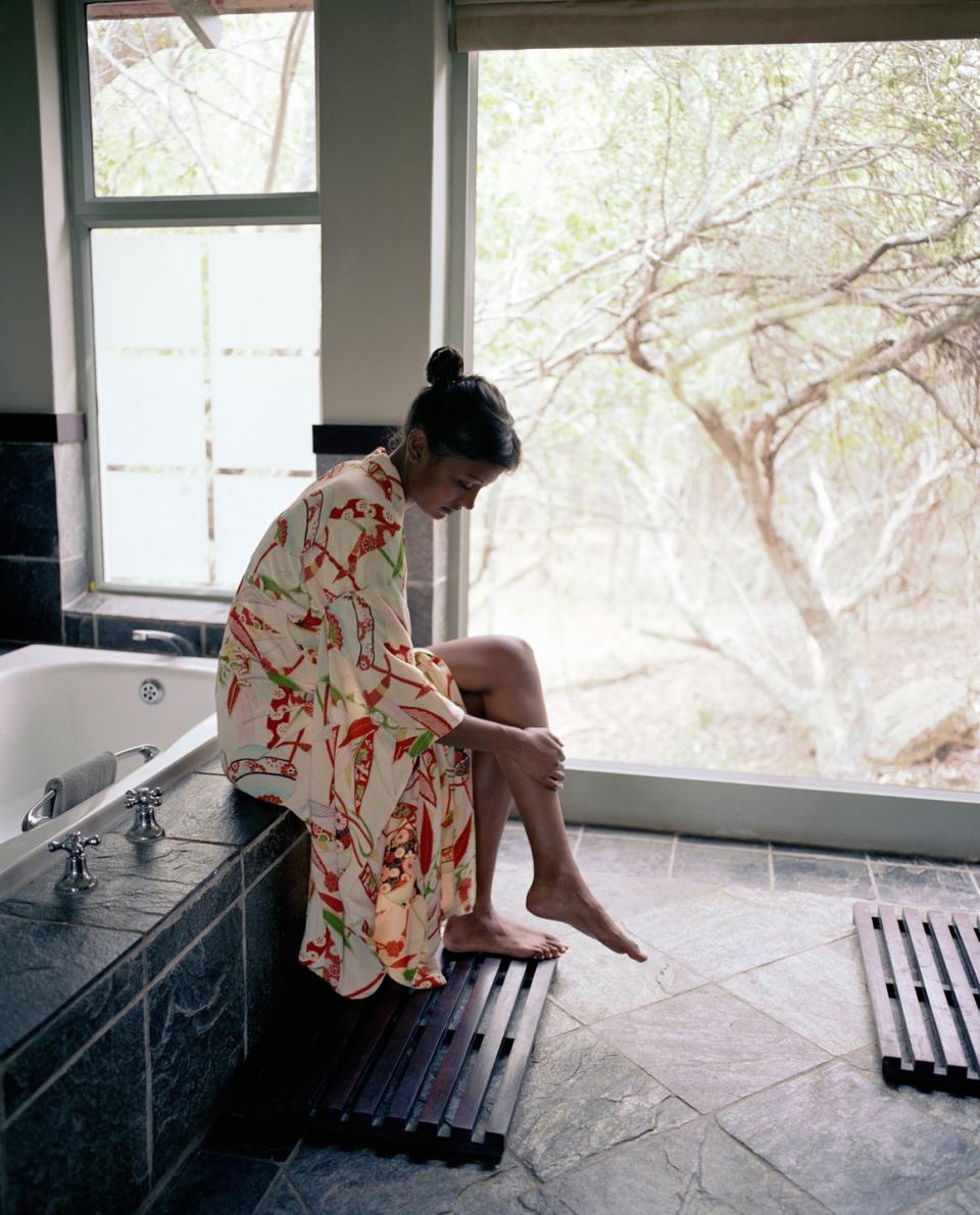 young woman sitting on bathtub ledge, touching shin, side view