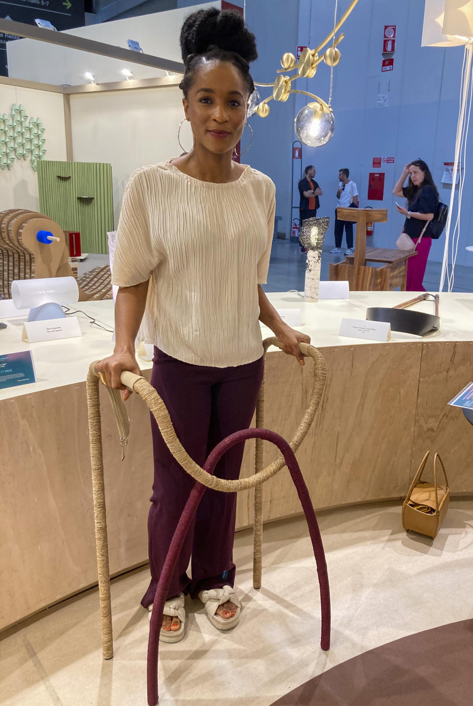 Nigerian designer Lani Adeoye poses with a walker she designed for her grandfather, who rejected the more standard medicinal-looking versions, in this picture taken Wednesday, June 9, 2022, at the International Furniture Fair grounds in Rho, near Milan, central Italy. An interlocking arch that represents unity gives her walker a sculptural flair, and the cording made out of water hyacinth connects both local artistry with sustainable materials. Adeoye's walker won the top prize at the Salone Satellite event. (AP Photo/Colleen Barry)