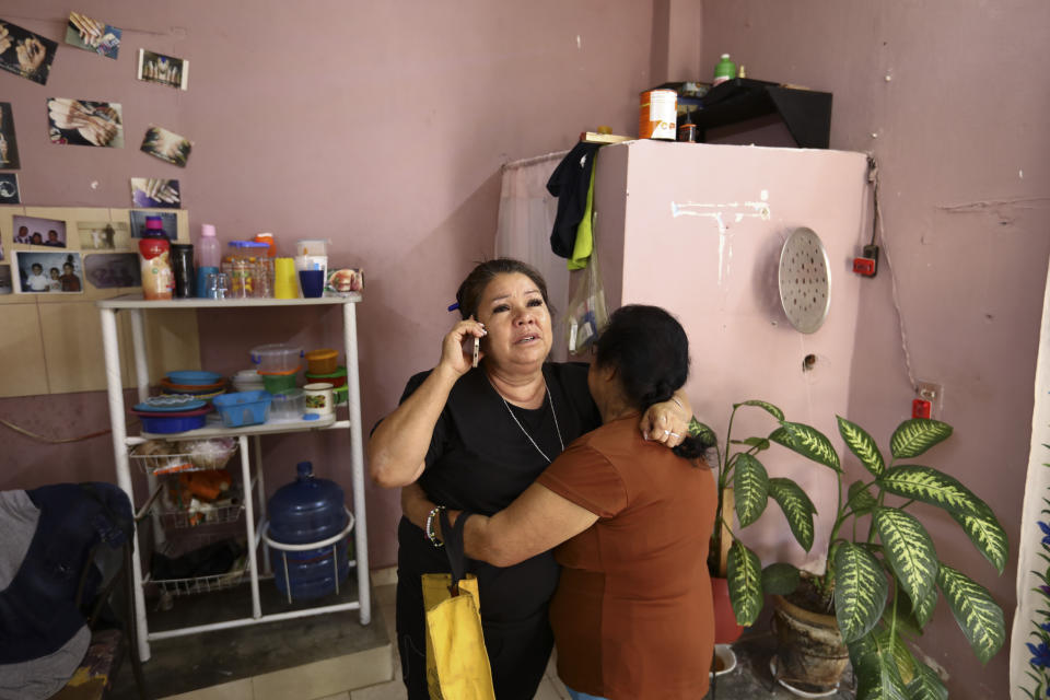 Rosa Alba Santoyo speaks on the phone and is embraced by a woman giving her condolences the day after she lost three of her adult children in an attack on the drug rehabilitation center where they were being treated, at her home in Irapuato, Mexico, Thursday, July 2, 2020. Gunmen burst into the drug rehabilitation center and opened fire Wednesday, killing 24 people and wounding seven, authorities said. After the loss of her three children, only two of Santoyo's seven children remain living. (AP Photo/Eduardo Verdugo)