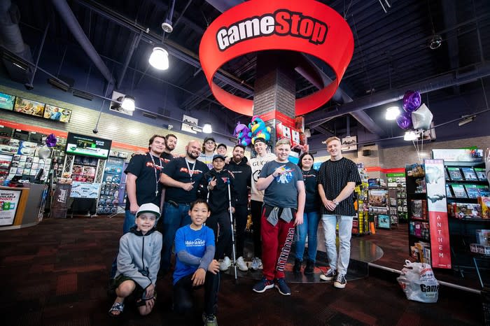 GameStop employees and fans pose inside a GameStop store.