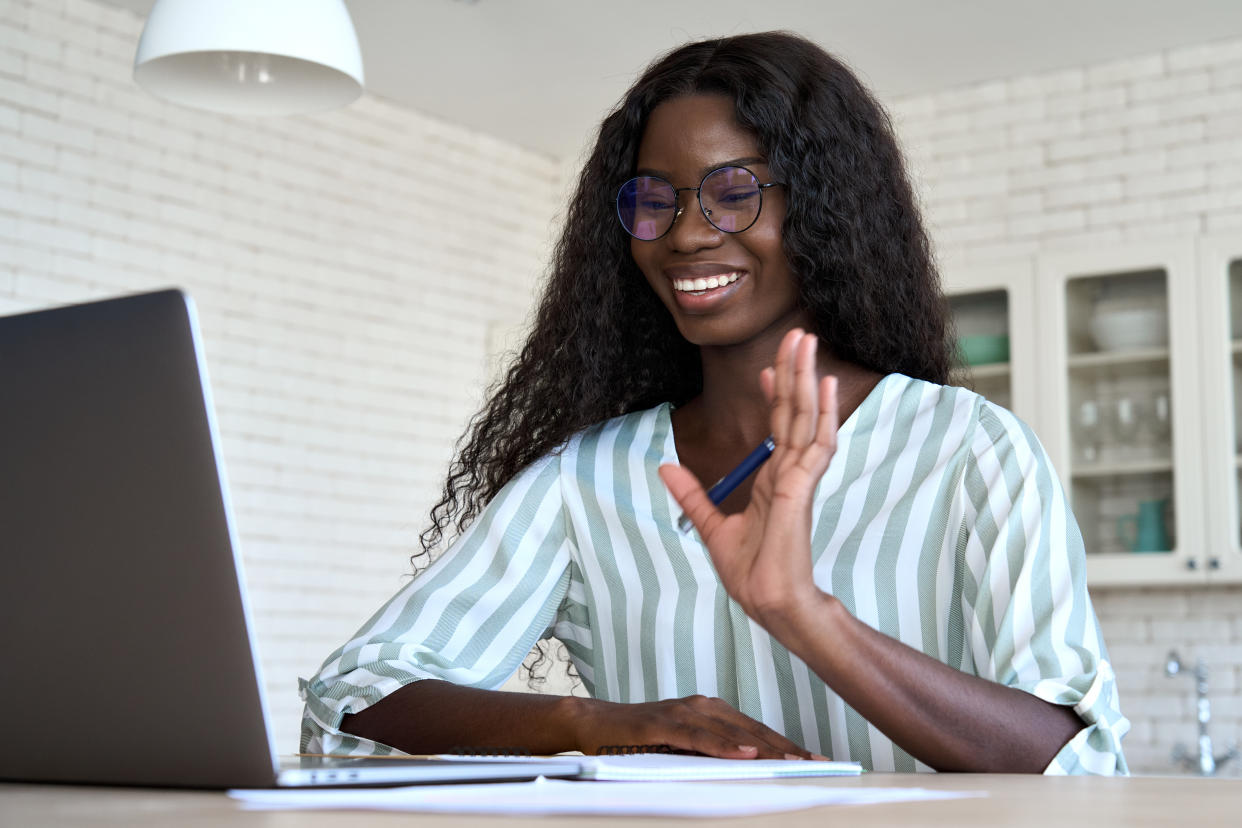 interview Happy young black woman student waving having video call virtual meeting distance working or learning at home looking at laptop computer talking by videocall digital conference.