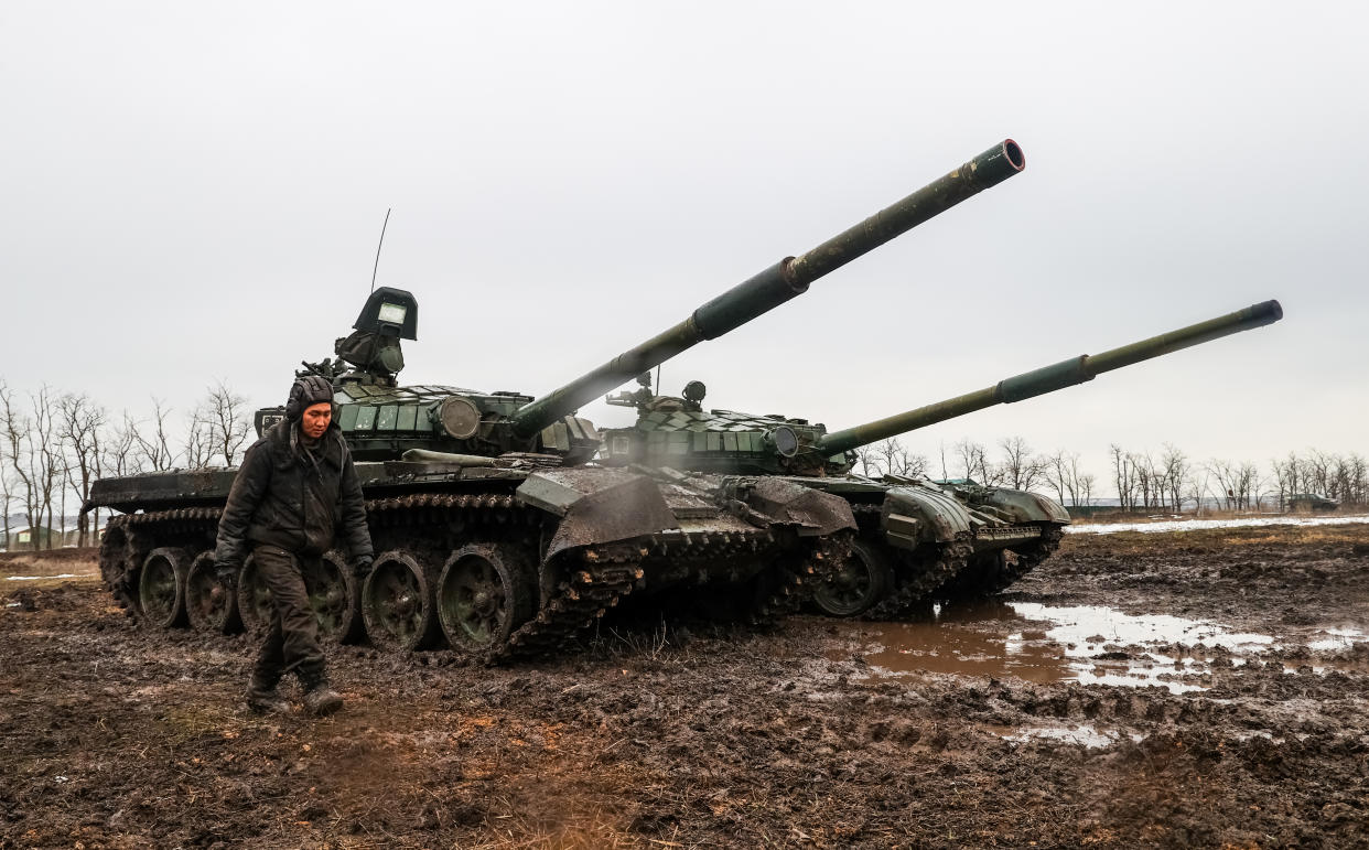 A man walks past two Russian tanks in a muddy field. 
