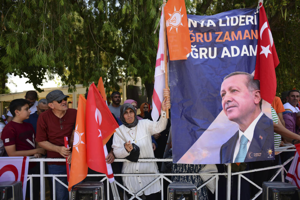 People hold a banner showing the Turkish President Recep Tayyip Erdogan, Turkish and Turkish Cypriot breakaway flags as they wait by a street side for his arrival, in the Turkish occupied area of the divided capital Nicosia, Cyprus, Monday, June 12, 2023. Erdogan is in the Turkish occupied area of north part of the Cyprus island on his first trip after his re-election after the May 28 presidential election. (AP Photo/Nedim Enginsoy)