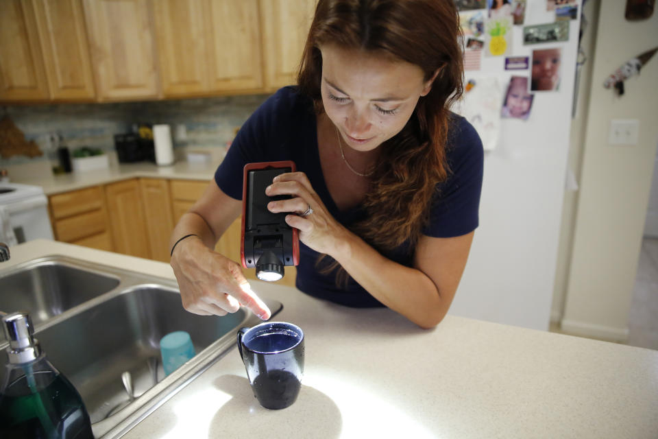 Lauren Wright, a Navy spouse whose family was sickened by jet fuel in their tap water, points out a sheen in a sample of tap water at her home in Honolulu, Friday, July 1, 2022. A Navy investigation says shoddy management and human error caused fuel to leak into Pearl Harbor's tap water last year. The leak poisoned thousands of people and forced military families to evacuate their homes for hotels. (AP Photo/Caleb Jones)