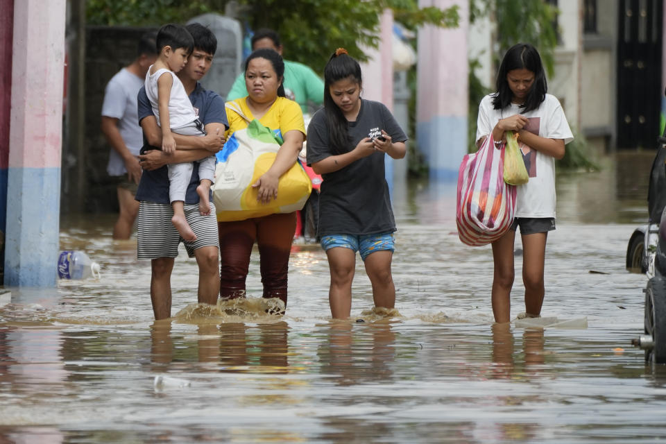 A family evacuates to higher ground as they wade through floodwaters from Typhoon Noru in San Miguel town, Bulacan province, Philippines, Monday, Sept. 26, 2022. Typhoon Noru blew out of the northern Philippines on Monday, leaving some people dead, causing floods and power outages and forcing officials to suspend classes and government work in the capital and outlying provinces. (AP Photo/Aaron Favila)