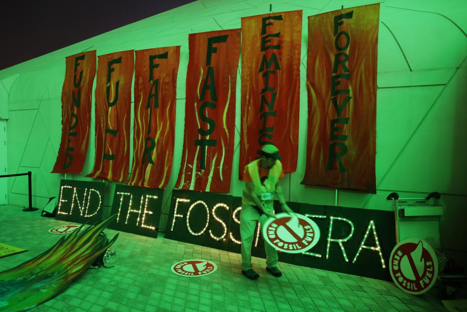 An activist places protest signs on the ground next to an illuminated sign that reads: 'End the fossil era’ (Getty Images)