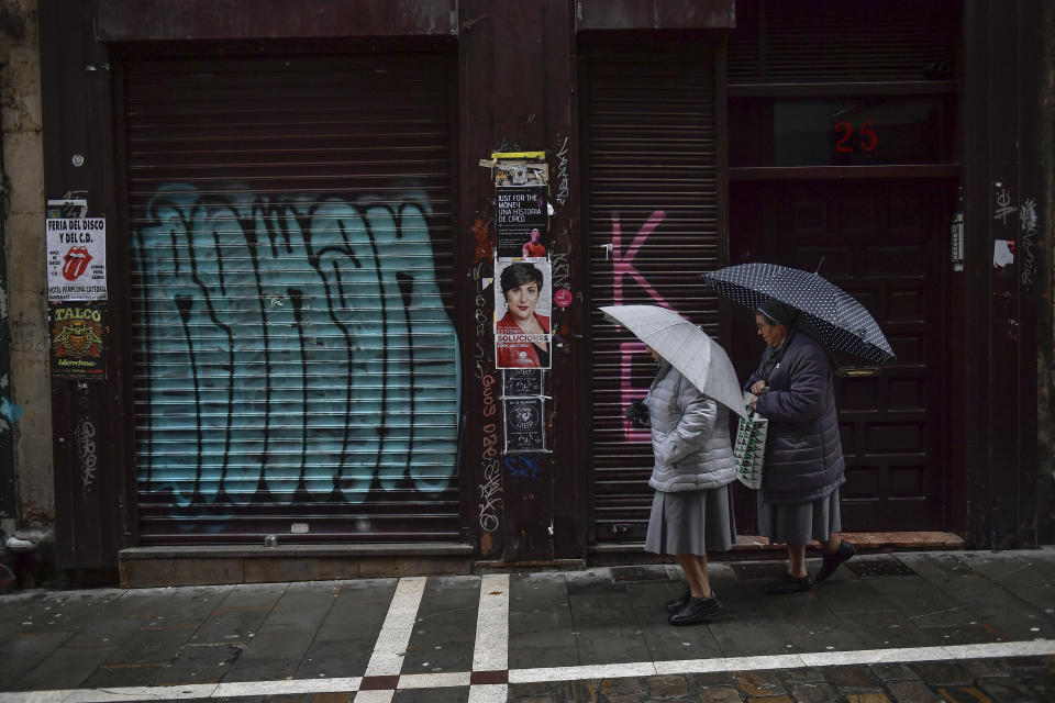Two nuns shelter under umbrellas while walking past a basque nationalist campaign cartel, center, the day after the general election, in Pamplona, northern Spain, Monday, Nov. 11, 2019. Spain looked set Monday to face political uncertainty for many more months after the country’s fourth elections in as many years further complicated an already messy political situation. (AP Photo/Alvaro Barrientos)