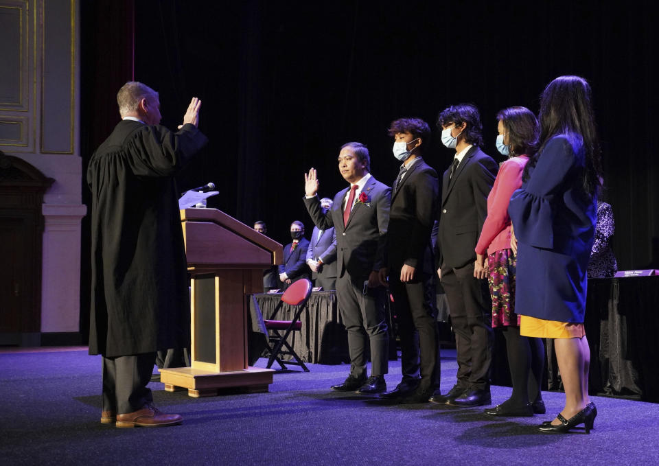 In this photo provided by Peg Shanahan, Lowell District Court Judge Stephen Geary, left, swears in new Mayor Sokhary Chau during the Lowell City Council swearing-in ceremony, Monday, Jan. 3, 2022, in Lowell, Mass., as Chau's family stands with him. Chau, a refugee who survived the Khmer Rouge’s bloody regime, has become the city’s first mayor of color and the first Cambodian American mayor in the United States. (Peg Shanahan via AP)