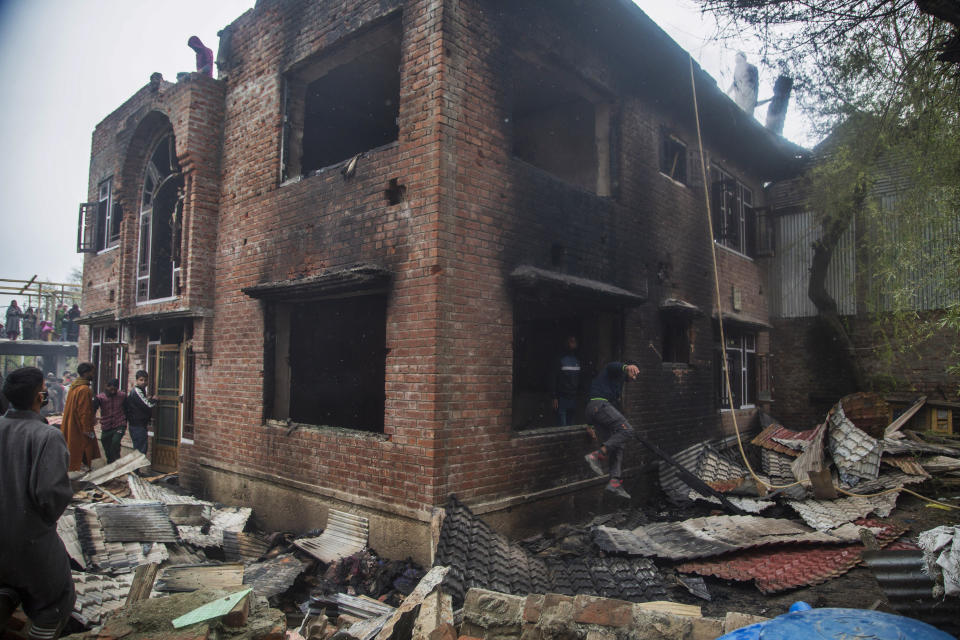 A Kashmiri man jumps through a window as villagers inspect a house that was damaged during a gun battle between government forces and suspected rebels in Bijbehara, some 28 miles (45 kilometers) south of Srinagar, Indian controlled Kashmir, Sunday, April 11, 2021. (AP Photo/Mukhtar Khan)