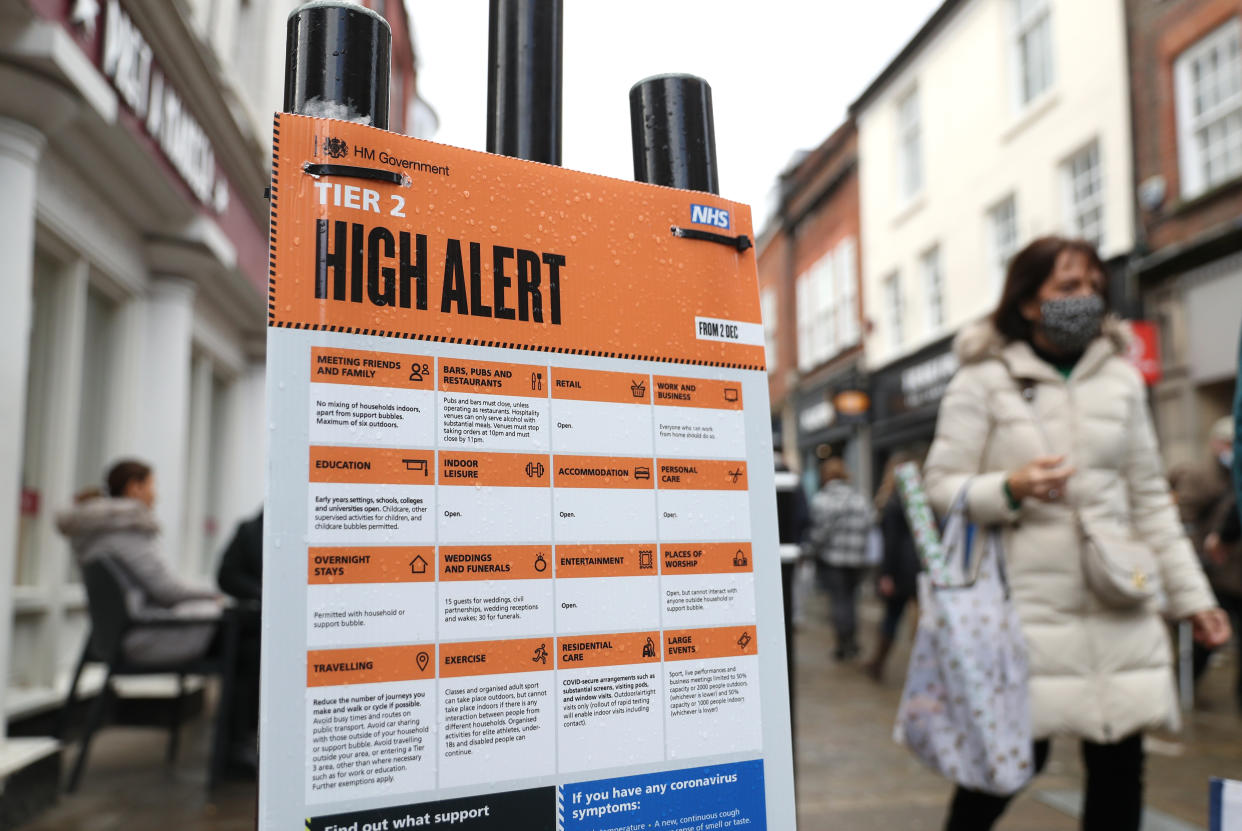 Christmas shoppers make their way past a Tier 2 High Alert sign the High street in Winchester, Hampshire. Downing Street has said that restrictions measures over the Christmas period were being kept under "constant review" in response to suggestions that the Christmas arrangements could be restricted to three days or two households. (Photo by Andrew Matthews/PA Images via Getty Images)