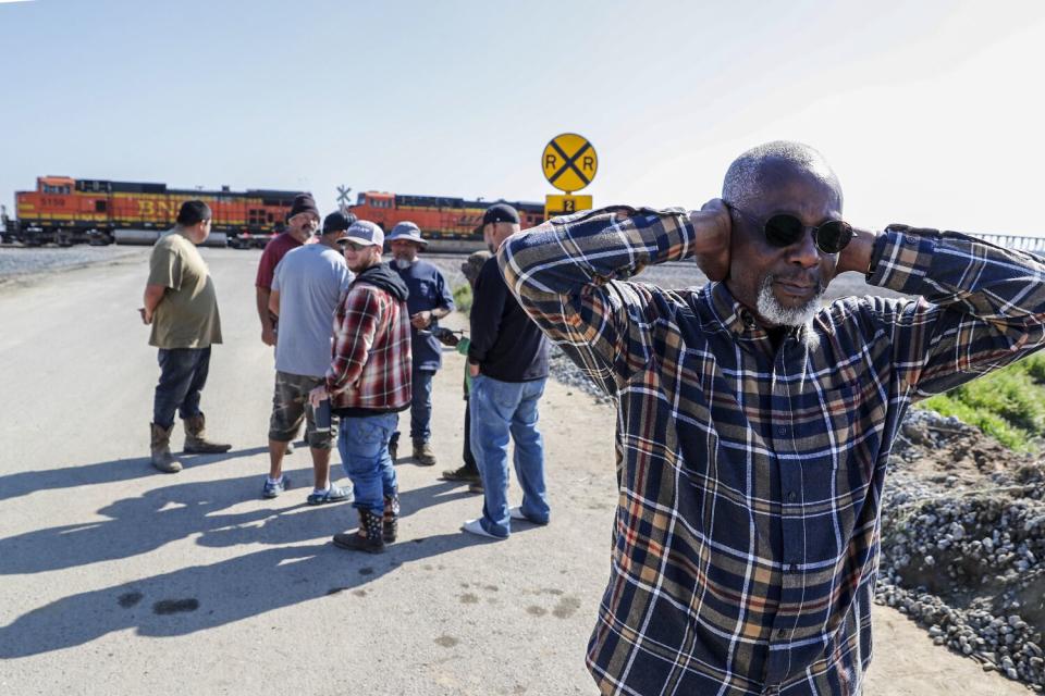 Kayode Kadara covers his ears as a freight train sounds its horn while passing a levy bridge residents fortified.