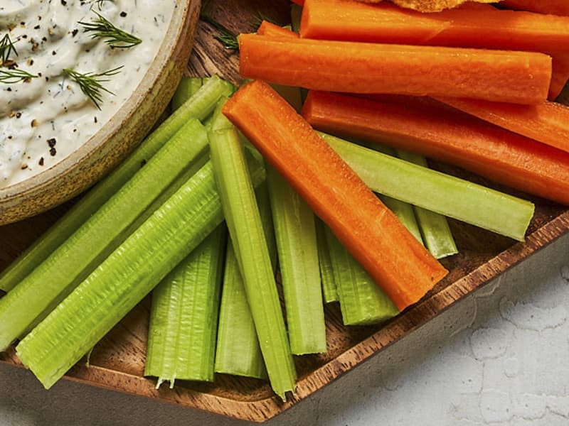 a bowl of creamy dill dip, on a plate with sliced carrots, celery and potato chips