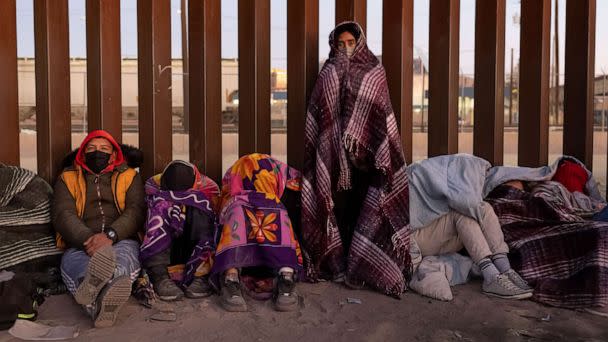 PHOTO: Immigrants bundle up against the cold after spending the night outside along the U.S.-Mexico border fence on Dec. 22, 2022, in El Paso, Texas. (John Moore/Getty Images)