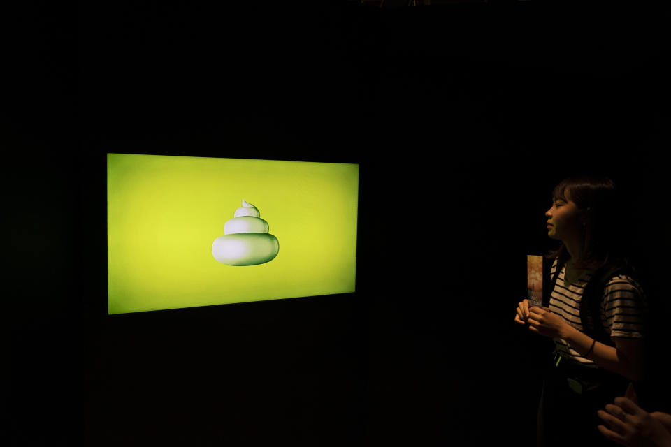 In this Tuesday, June 18, 2019, photo, a woman watches a clip while waiting to enter the Unko Museum in Yokohama, south of Tokyo. In a country known for its cult of cute, even poop is not an exception. A pop-up exhibition at the Unko Museum in the port city of Yokohama is all about unko, a Japanese word for poop. The poop installations there get their cutest makeovers. They come in the shape of soft cream, or cupcake toppings. (AP Photo/Jae C. Hong)